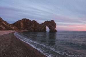 Durdle Door rock formation on Dorset coast at sunset, tranquil seascape with pink skies.